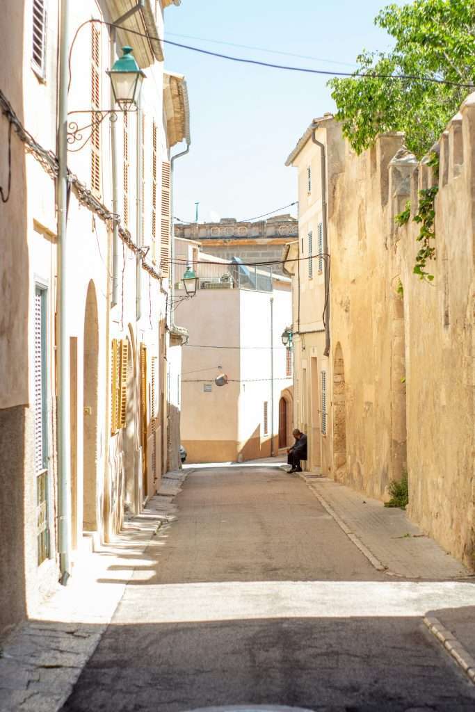 Calle tranquila en un pueblo, con una persona descansando a la sombra, representando la tradición de la siesta en un entorno urbano.