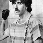 Charly García en una fotografía en blanco y negro, levantando el puño mientras usa guantes.